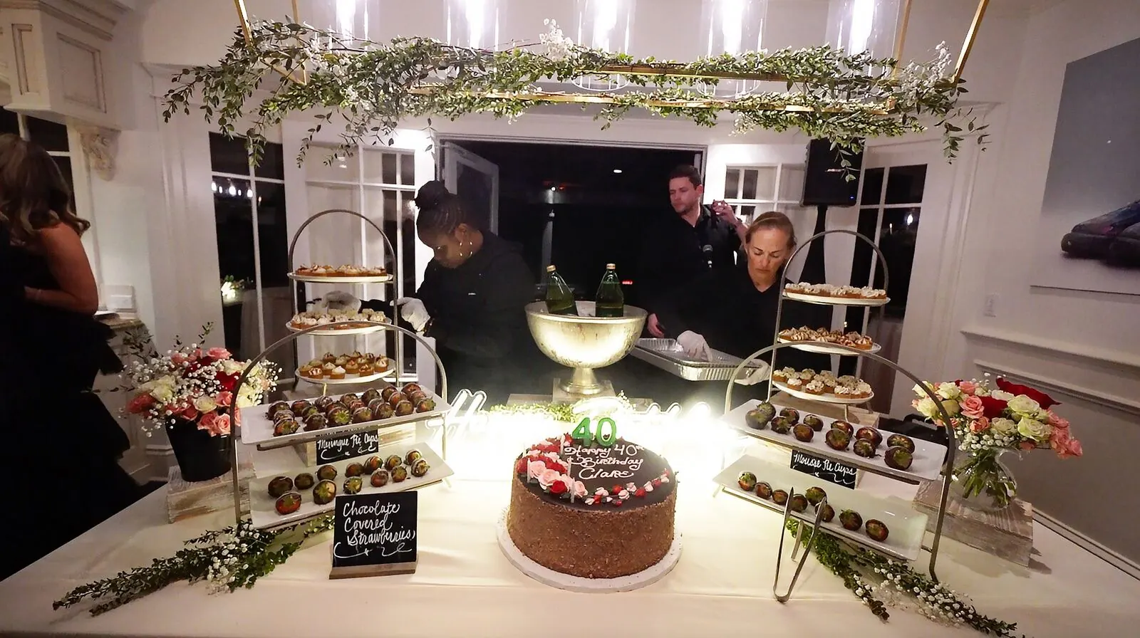 Dessert table of dipped strawberries, layered cake and petite sweets accented with fresh blooms on tiered risers — floral dessert styling for San Mateo catering